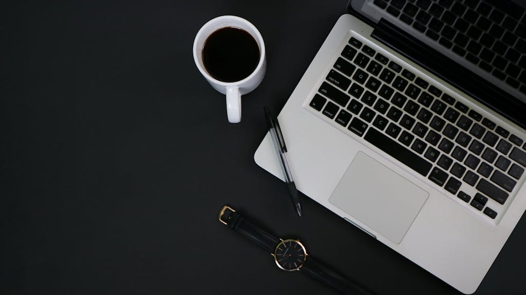 A clean workspace with a laptop, coffee, pen, and watch, ideal for productivity and focus.