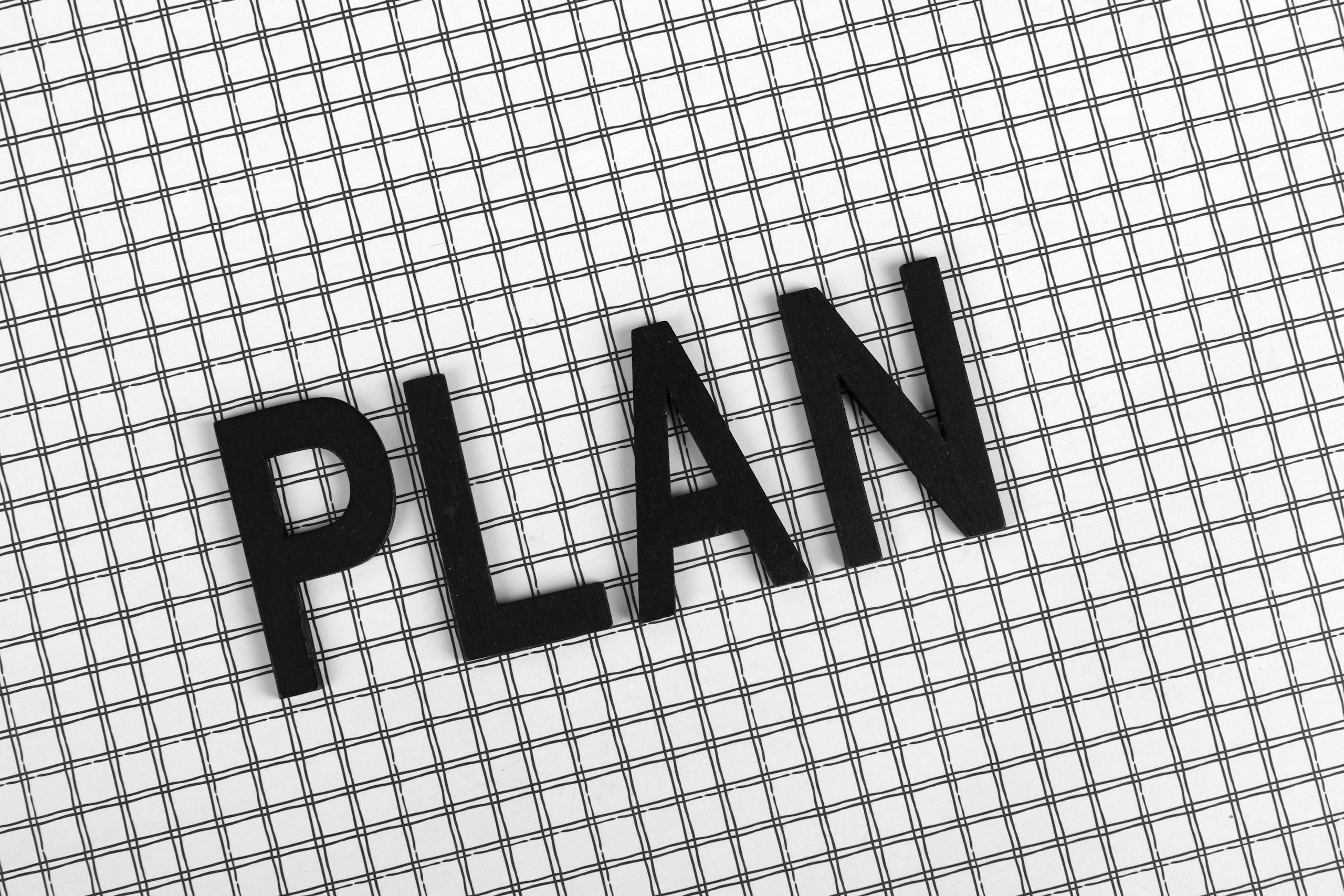 Black wooden letters spelling 'PLAN' on a checkered pattern background.